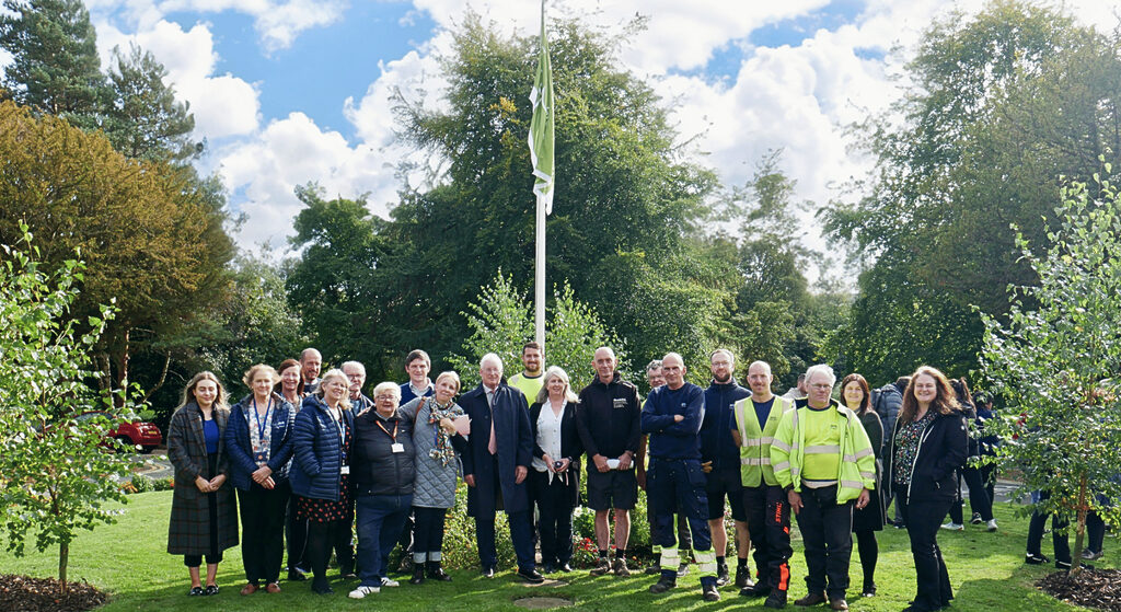 Hospital staff and visitors stand in front of the Green Flag at the Royal Edinburgh Hospital