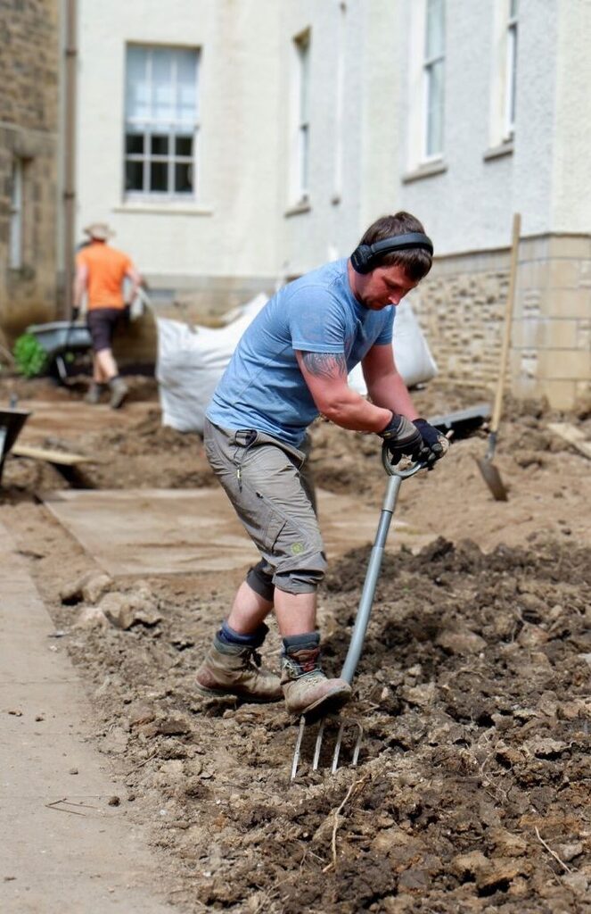 Gardener wearing a blue top digging up the soil at Woodland House