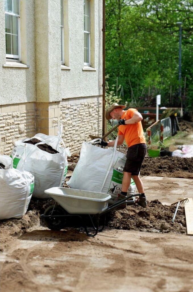 Gardener wearing a orange top digging up the soil at Woodland House