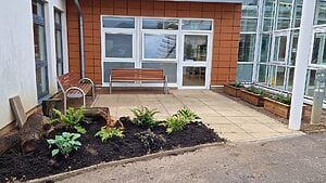 Outside the reception area of the SMART Centre. There are two benches on a patioed area with a planters and an area of newly planted flowers and greenery