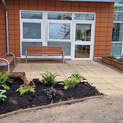 Outside the reception area of the SMART Centre. There are two benches on a patioed area with a planters and an area of newly planted flowers and greenery