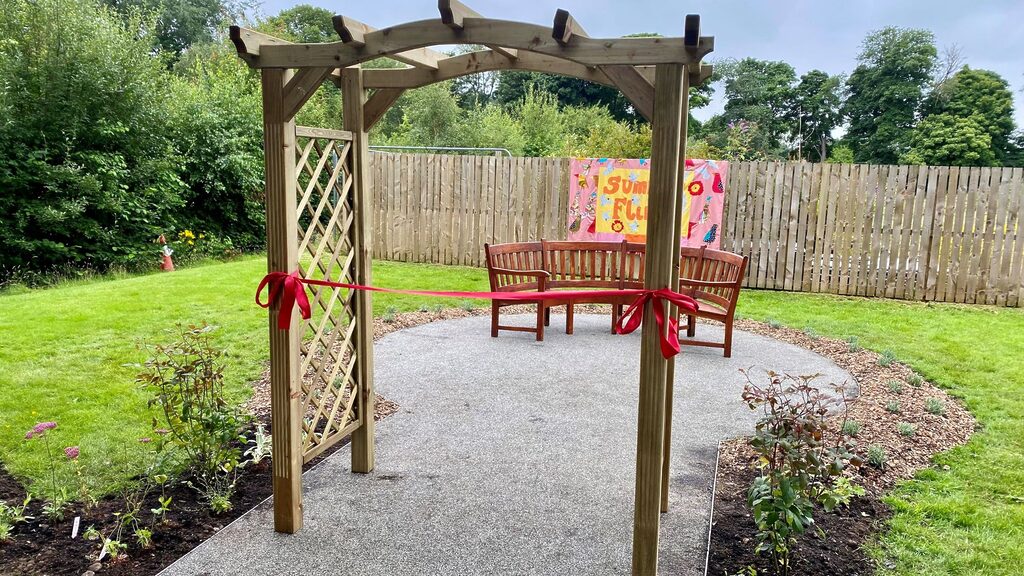 Photo of the new accessible path at the Royal Edinburgh Hospital. You can see a red ribbon ready to be cut to open the path in the foreground and a bench and flowers in the background.