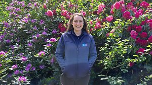 RSPB Nature and Wellbeing Officer, Beth Cochrane standing in front of purple and pink flowering bushes