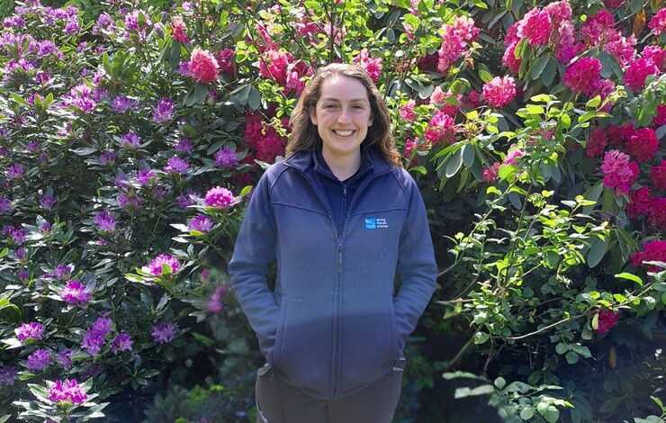 RSPB Nature and Wellbeing Officer, Beth Cochrane standing in front of purple and pink flowering bushes