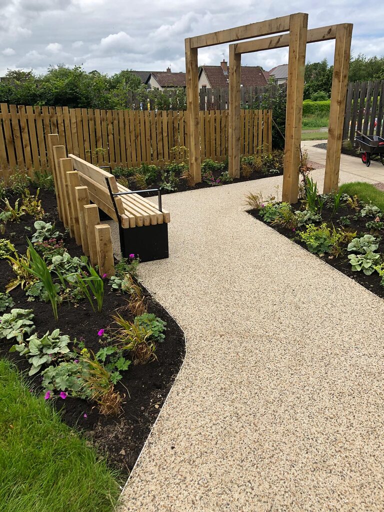 a gravel path with a bench and pergola arches with planting along the edges
